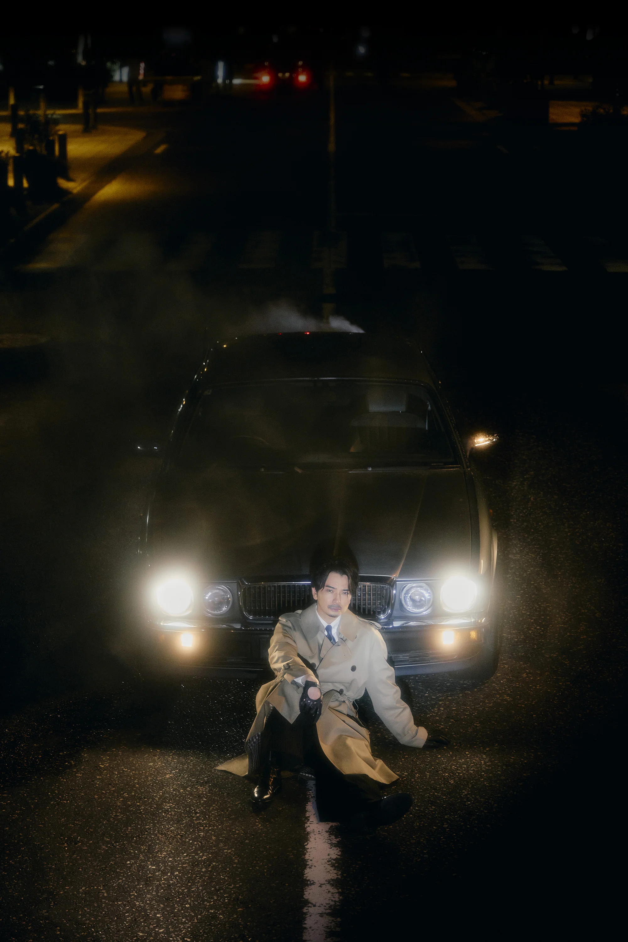 Jun Matsumoto seated in front of a car with its headlights on